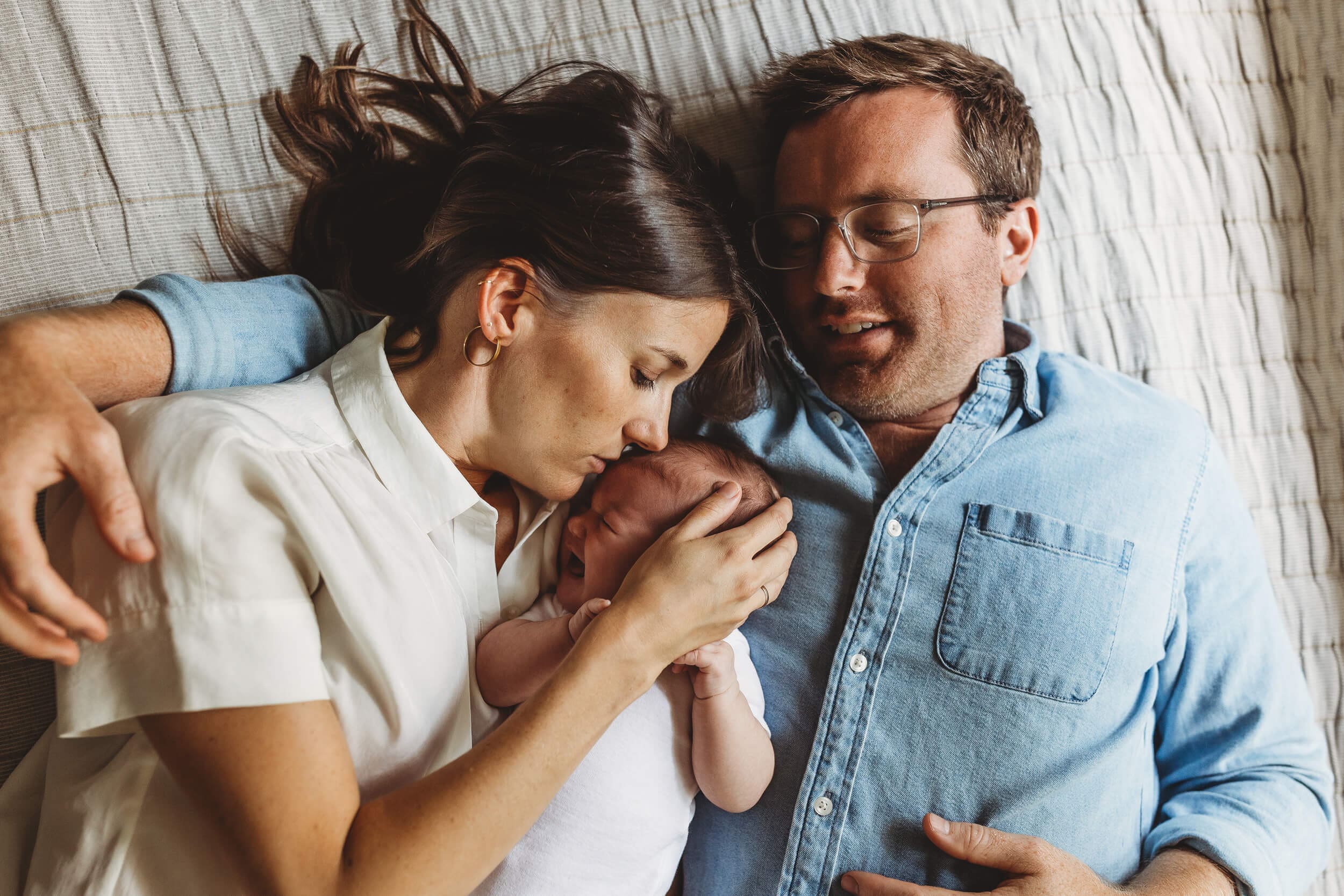Parents laying on bed with newborn baby during intimate in-home newborn photography session