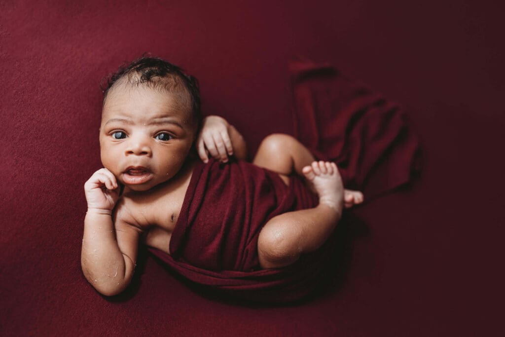 Awake baby boy in rich berry wrap during a posed newborn session with an Atlanta newborn studio photographer