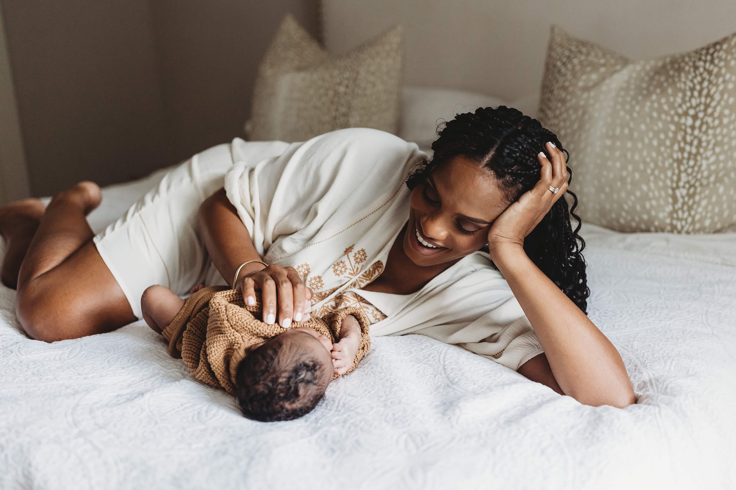 Mother resting on bed with her newborn baby in soft natural light, capturing a quiet postpartum moment at home