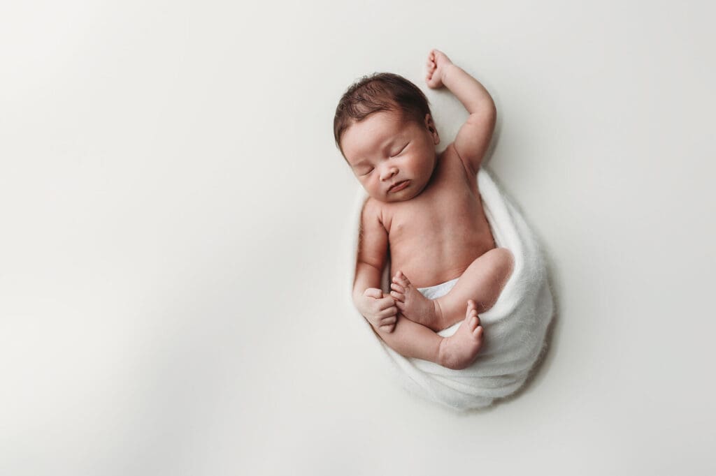 Atlanta newborn studio photographer capturing a sleepy newborn in a simple white wrap during a relaxed, baby-led posed session