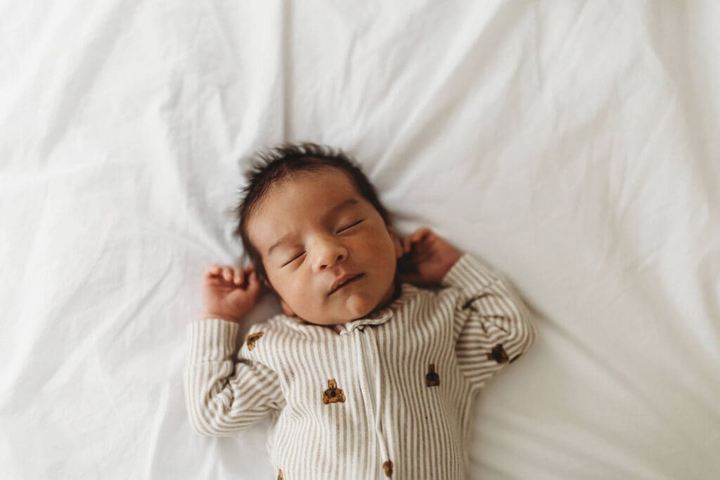 Marietta newborn photographer capturing sleeping baby laying on bed with arms up wearing cozy pajamas during in-home session