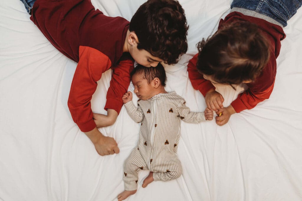 Marietta newborn photography session with older brothers laying on bed looking at their new baby brother during in-home session