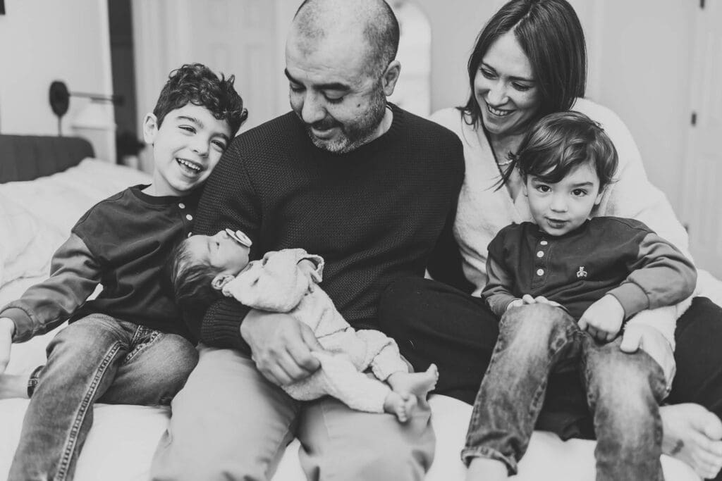 Atlanta newborn photographer capturing black and white candid photo of family with three boys laughing and snuggling on bed