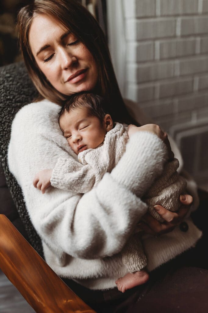 Atlanta in-home newborn photography session with mom snuggling baby by window light, neutral knit outfit, studio setup brought to home