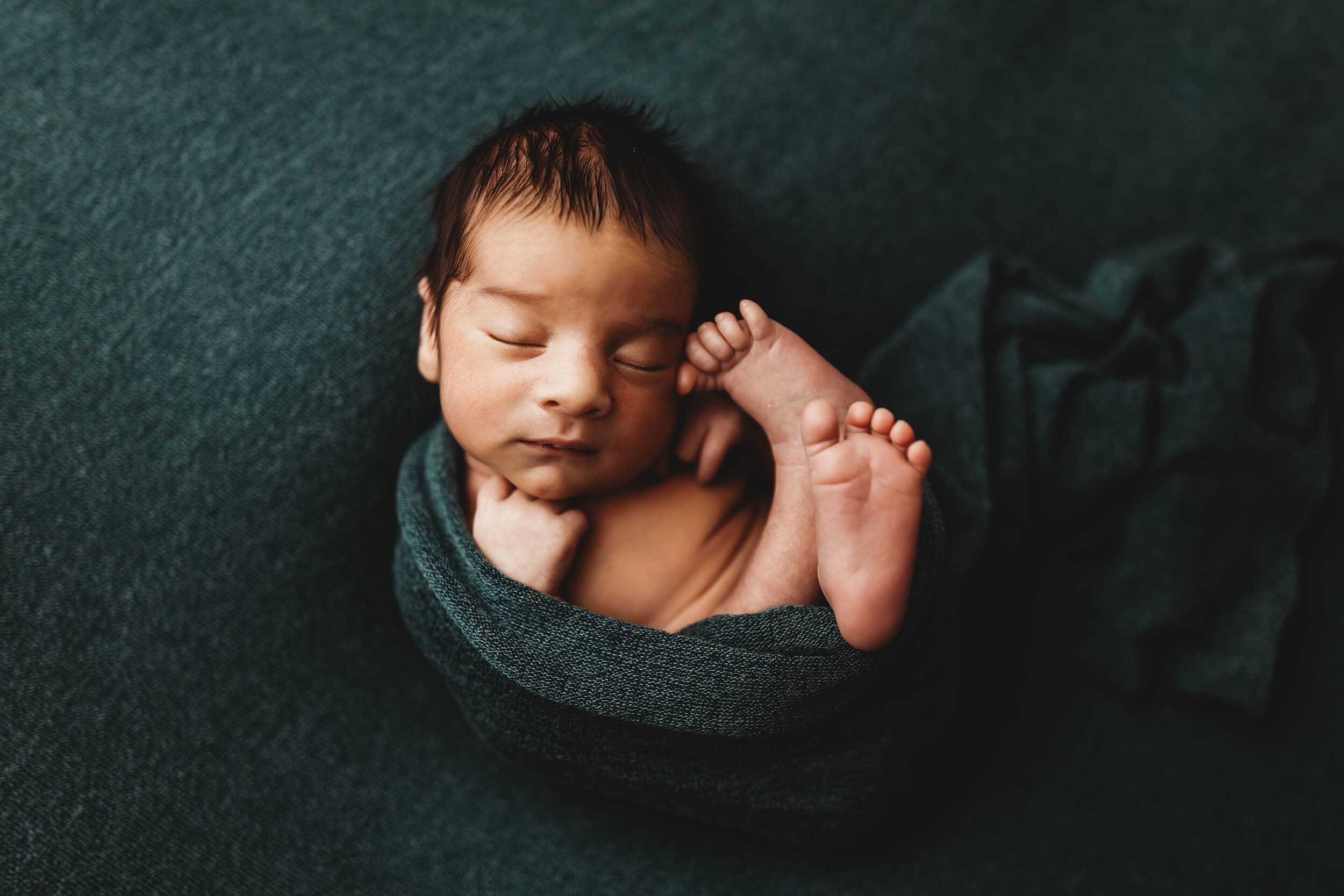 Newborn baby wrapped in rich teal fabric during studio session with Marietta newborn photographer, timeless posed portrait