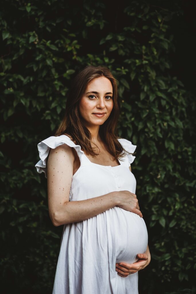 Fine art maternity portrait in Atlanta of expecting mother in white dress gently holding her baby bump