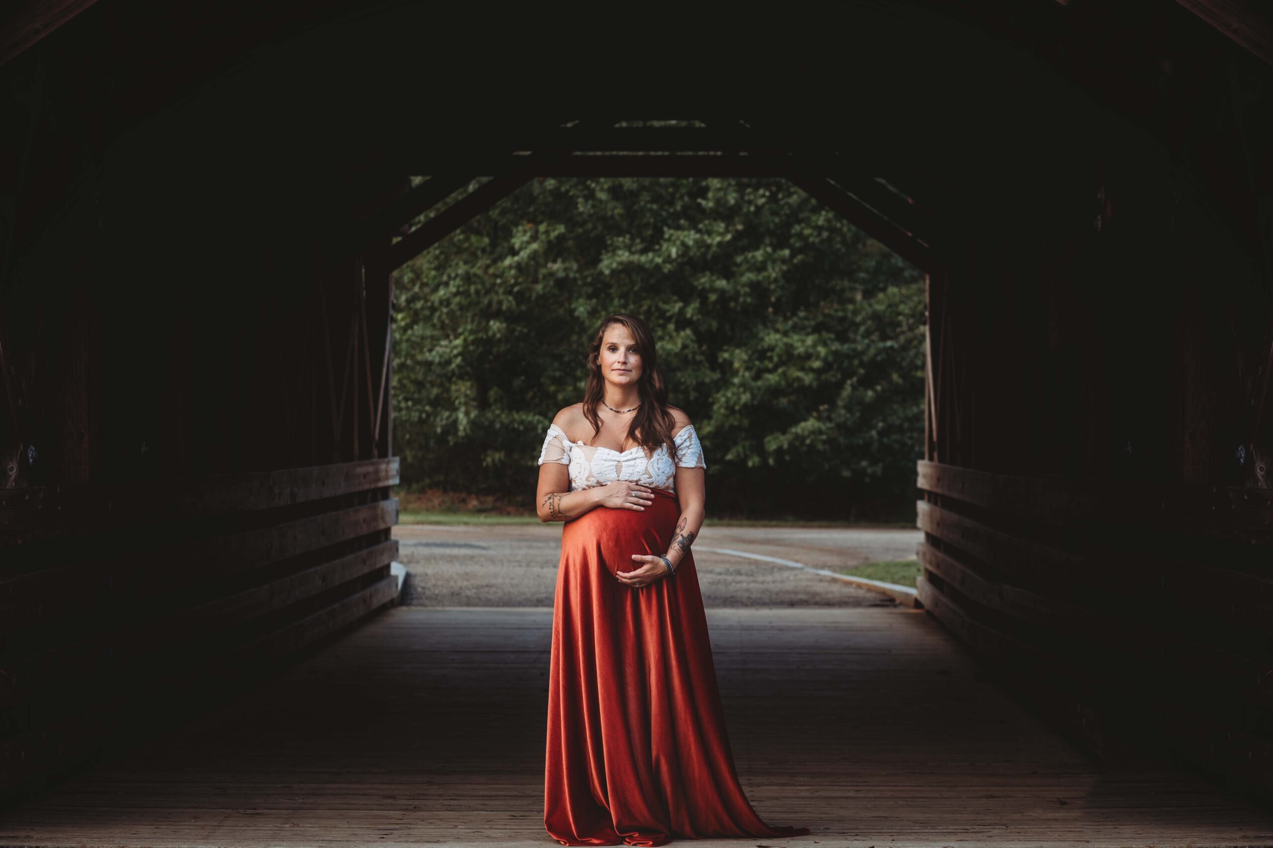 Atlanta maternity photographer capturing expectant mother in a red velvet long skirt cradling her belly at Garrard Landing Park in Roswell GA during golden hour