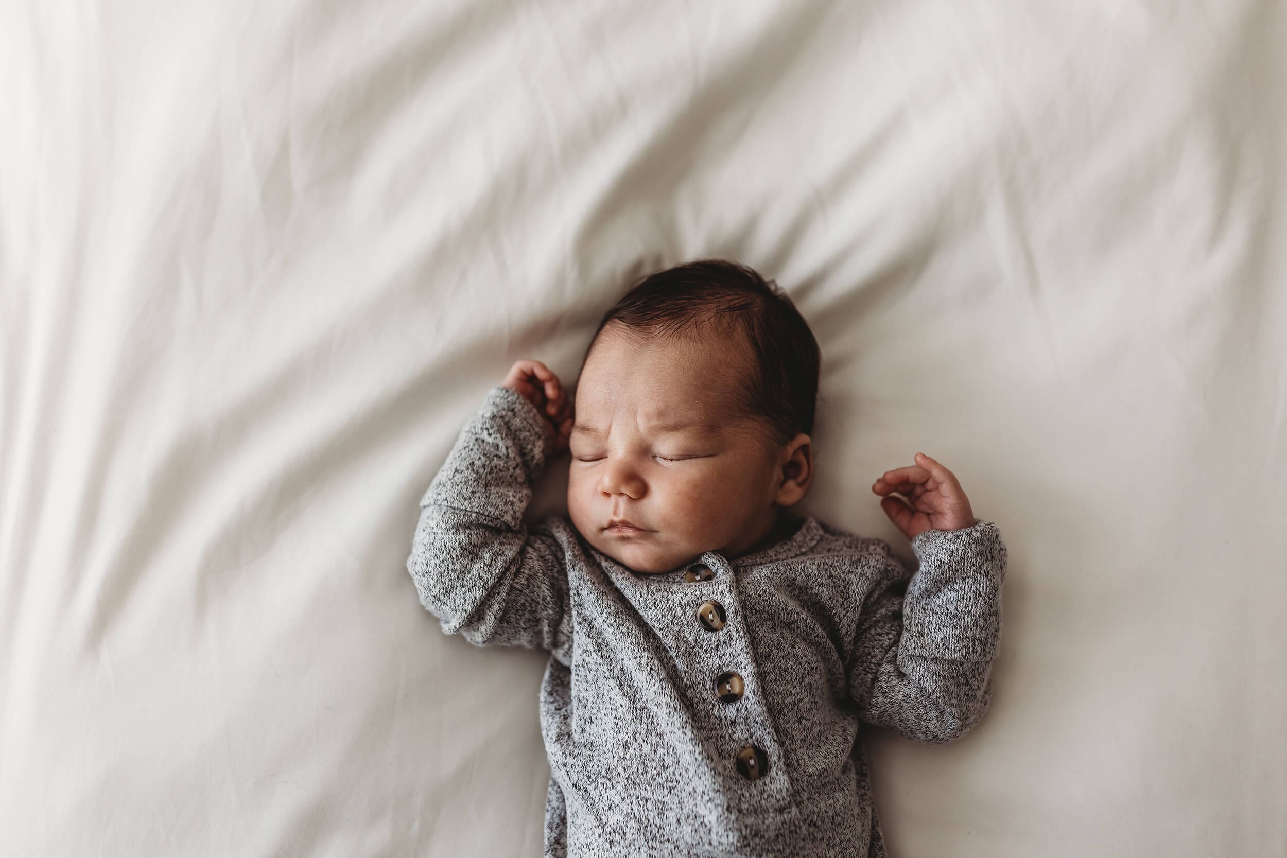 Sleepy newborn baby boy lying on a bed during a Roswell photography session.