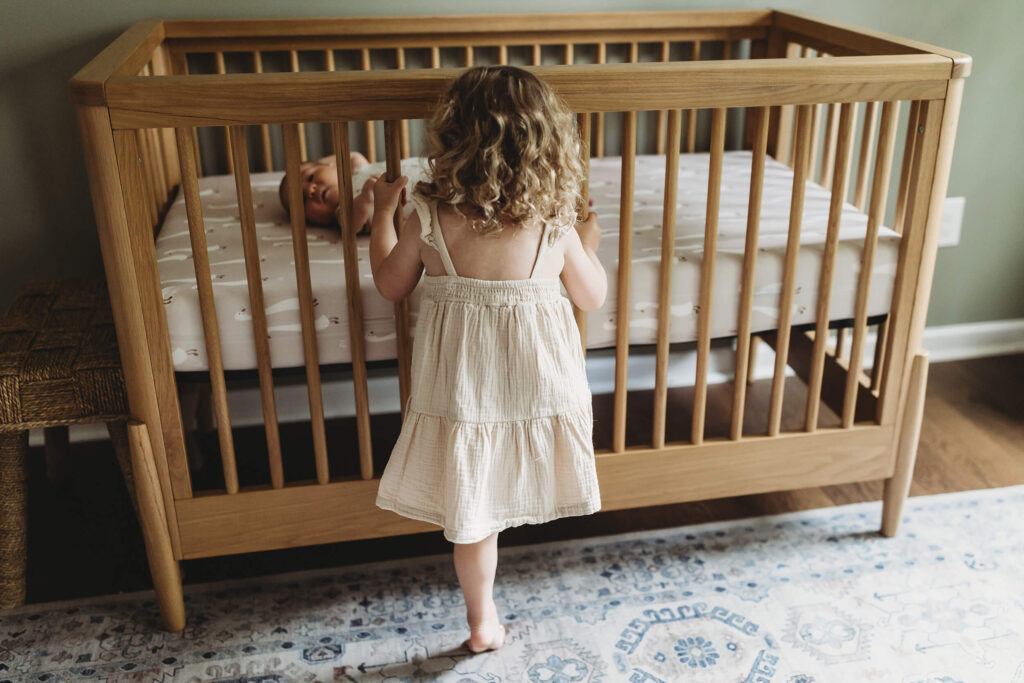 n-home newborn session Atlanta toddler sister looking at baby in crib candid moment