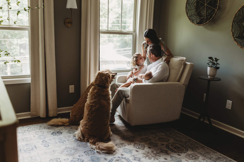 Atlanta newborn photographer documentary family portrait by window light with parents holding newborn and toddler with golden retrievers