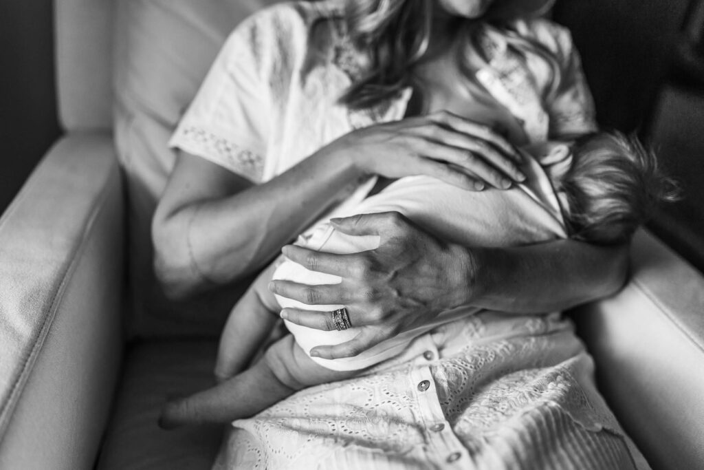 Black and white portrait of a mother peacefully breastfeeding her baby in a chair during early postpartum days