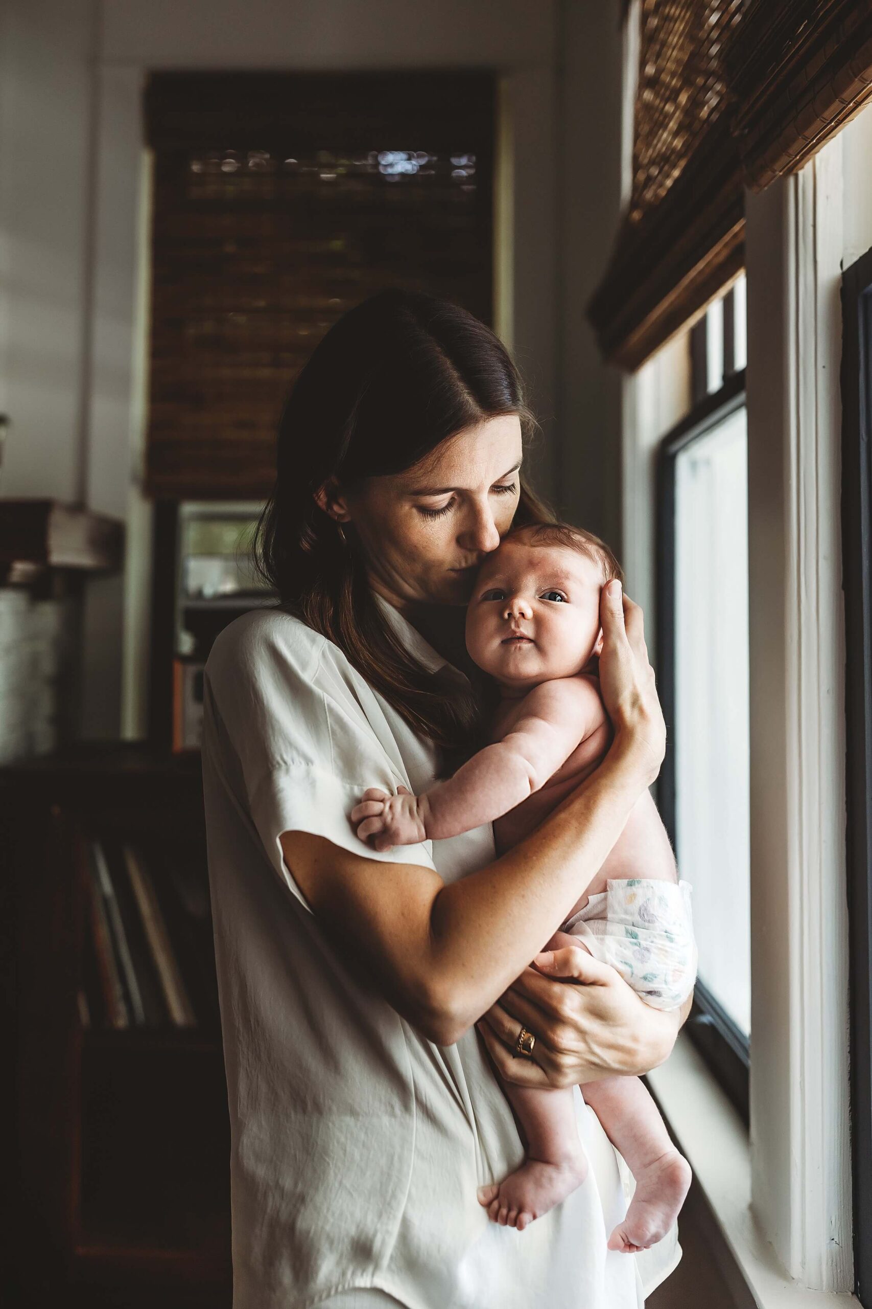 Mother holding newborn by window light during Atlanta in-home newborn photography session
