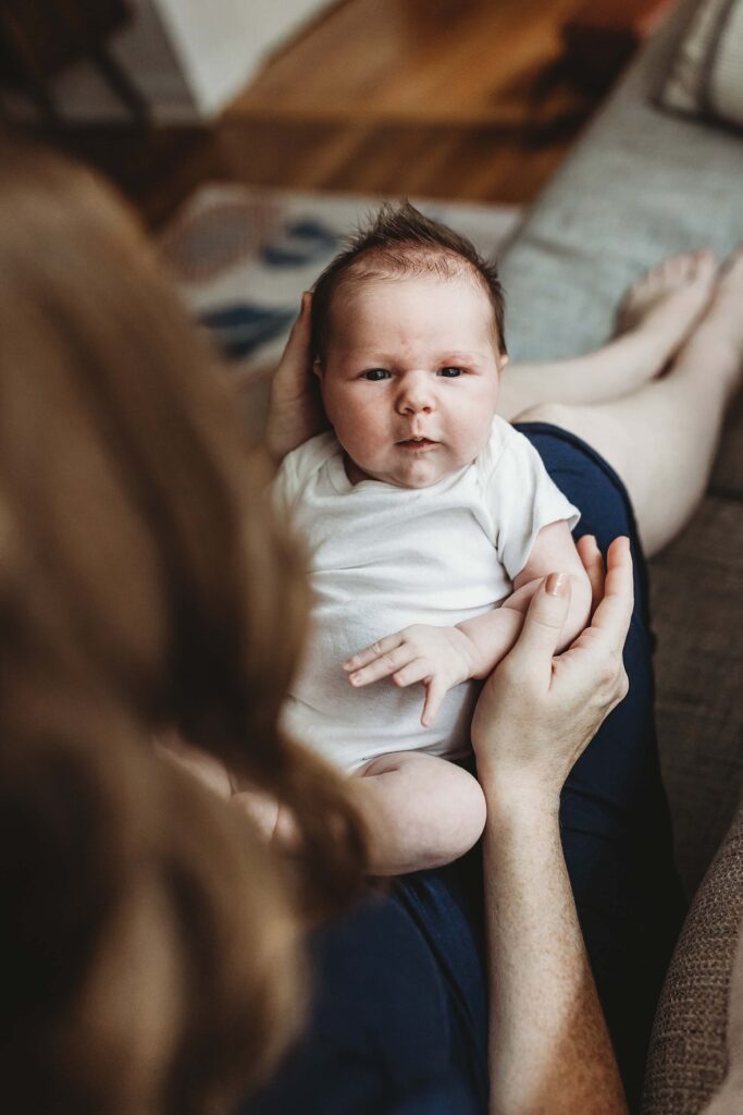 Atlanta newborn photographer capturing older baby resting in mother’s lap looking at camera during in-home session