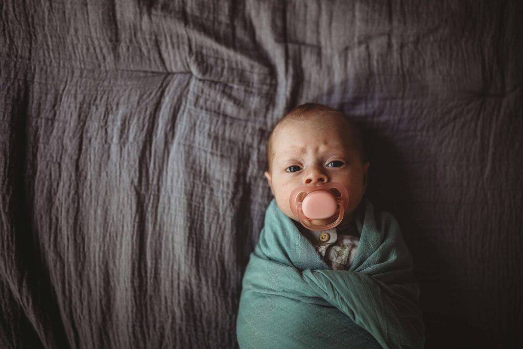 Atlanta newborn photography of baby looking at the camera with pacifier, tightly wrapped in soft swaddle