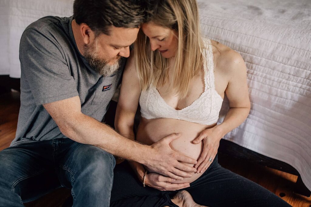 In-home maternity photo of Atlanta couple sitting on the floor with hands on pregnant belly
