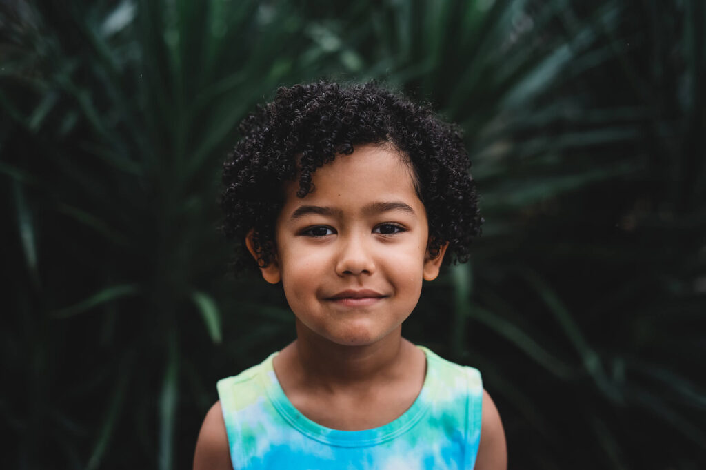 Curly-haired boy in a blue tank top shyly looking at the camera, natural child portrait
