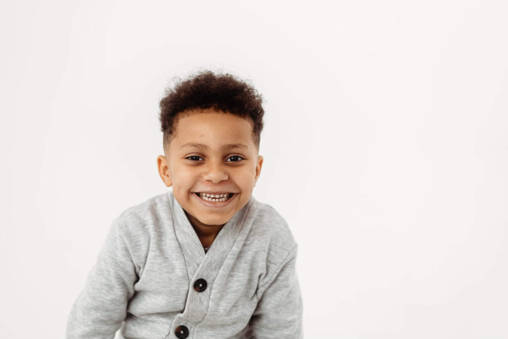 Curly-haired boy wearing a cardigan against a white background, natural child portrait