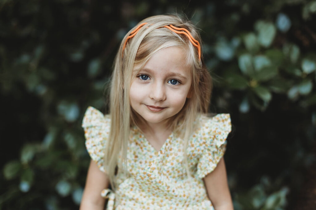 Girl in a yellow floral dress smiling naturally, relaxed child portrait