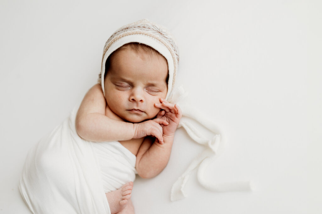Newborn baby wrapped in white with a textured bonnet during a simple newborn session Atlanta GA studio setup at home.
