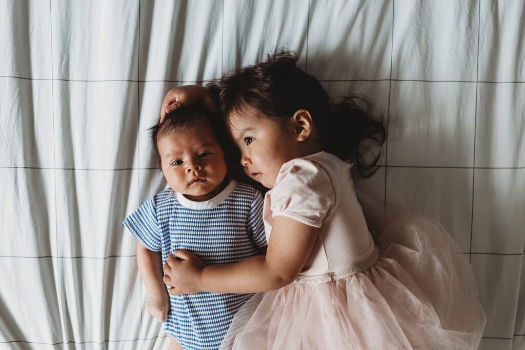 Decatur lifestyle newborn photographer capturing a quiet moment of big sister snuggling her newborn baby brother on the bed, natural sibling connection during an in-home newborn session in Atlanta, Georgia