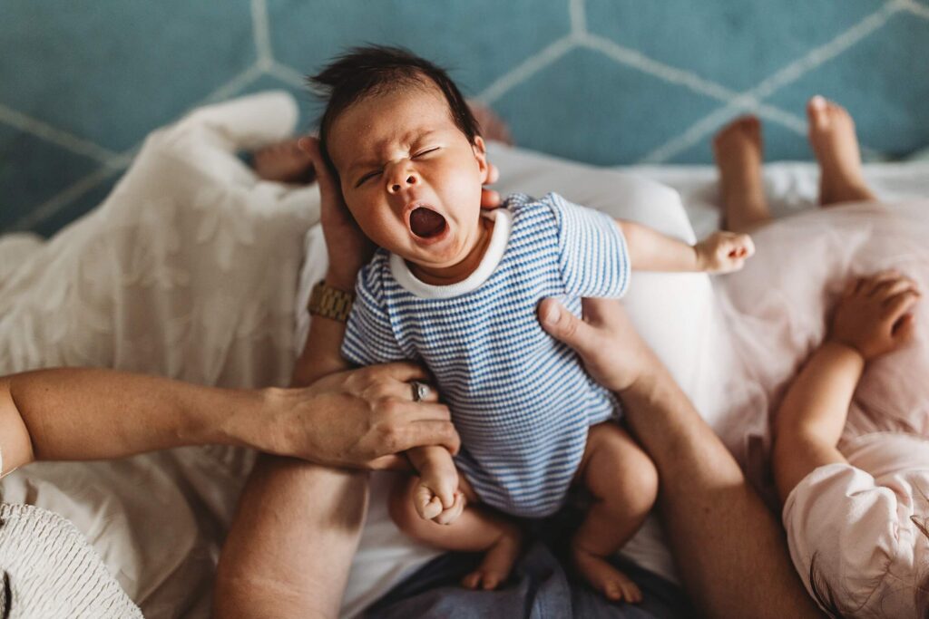 Decatur newborn photography capturing a baby resting in a parent’s lap and yawning—a sweet candid moment from an in-home lifestyle newborn session in Atlanta, Georgia, alongside a thoughtful resource for families considering a sleep consultant.