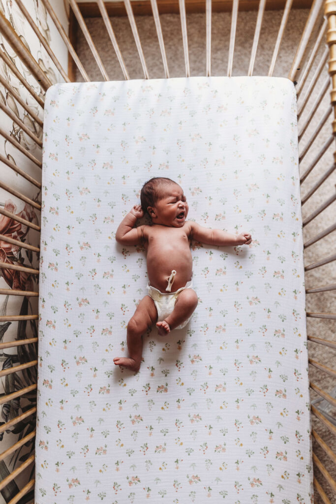 Baby lying peacefully in a crib surrounded by soft neutral bedding in a light-filled nursery, styled for timeless newborn photography in Atlanta
