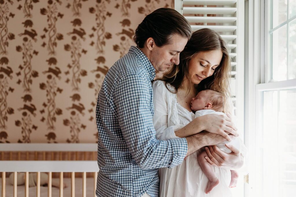 Intimate family portrait with parents holding their newborn by soft window light during an in-home newborn photography session in Atlanta, Buckhead