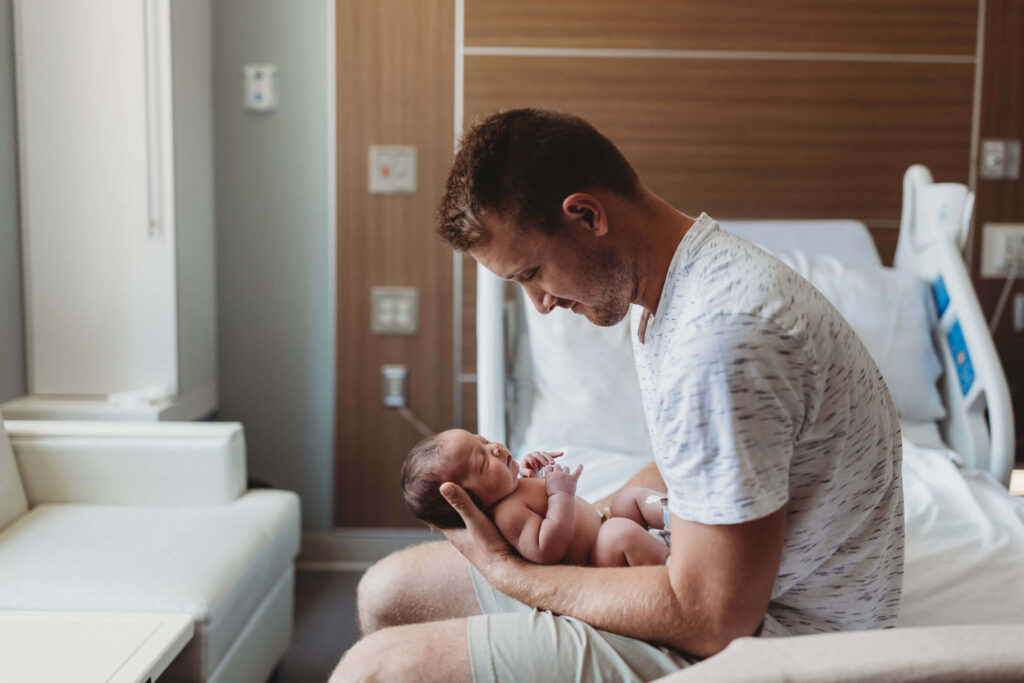 Dad holding his newborn baby during a Fresh 48 session at Piedmont Hospital, sharing a quiet moment in the hospital room with soft natural light and an intimate Atlanta birth story feel.