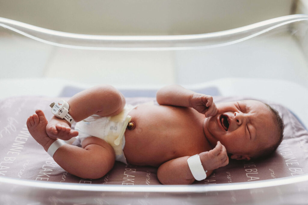 Newborn baby resting peacefully in a hospital bassinet during a Fresh 48 session at Piedmont Hospital in Atlanta, wrapped in a white swaddle with soft hospital lighting and a calm, intimate atmosphere.