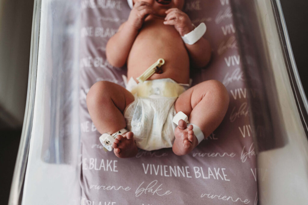 Detail shot of a newborn’s tiny feet peeking out from a diaper and wrapped in a custom baby blanket during a Fresh 48 session at Northside Hospital.