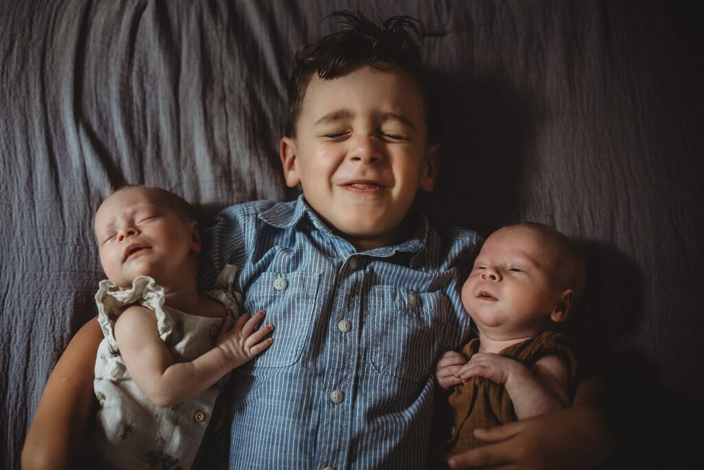 Big brother laying on bed with newborn twins during in-home newborn session in Sandy Springs