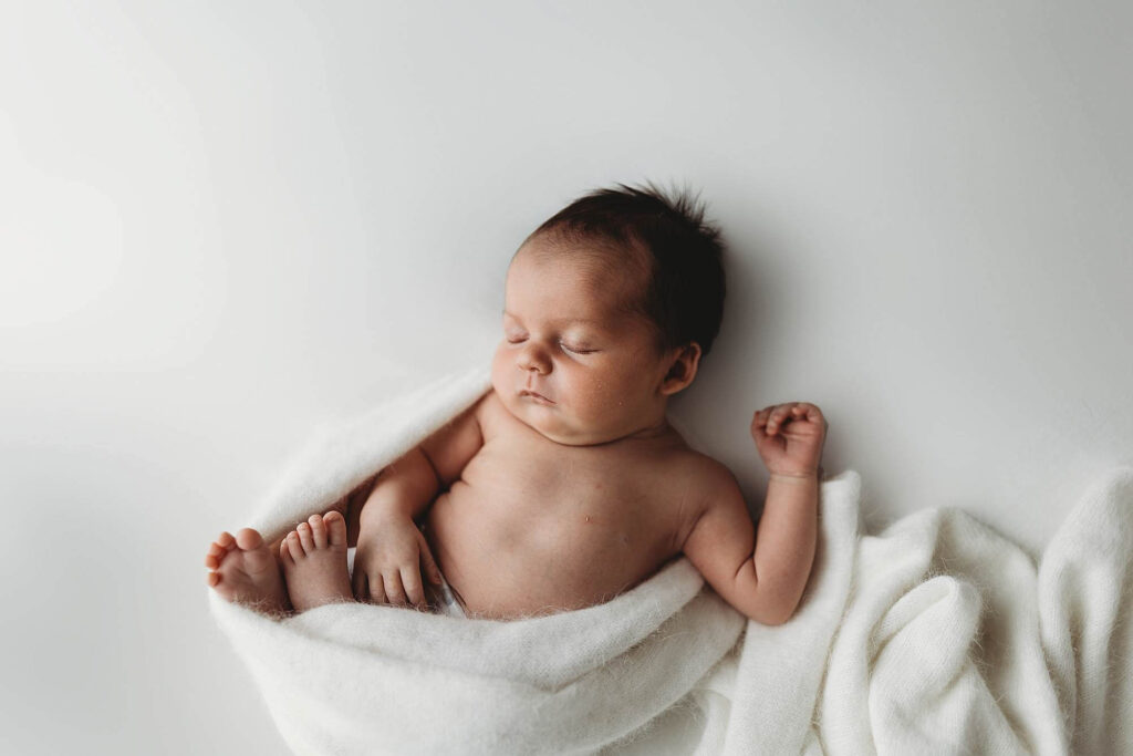 Newborn baby in a relaxed baby-led pose wrapped in soft white cashmere during an Atlanta newborn photography session.