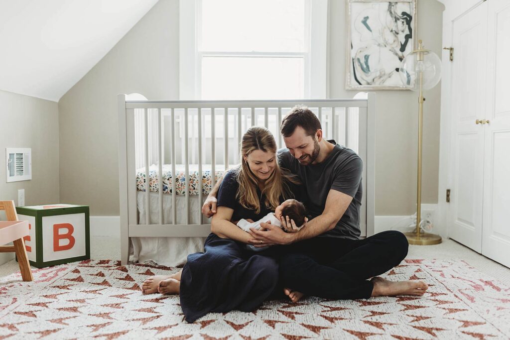 Wide-angle view of first-time parents sitting on the nursery floor with their newborn during an Atlanta in-home newborn photography session.