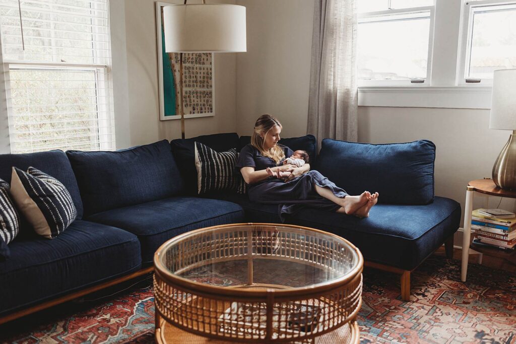 Mother sitting on a cozy living room couch looking at her newborn baby during an Atlanta lifestyle newborn photography session.