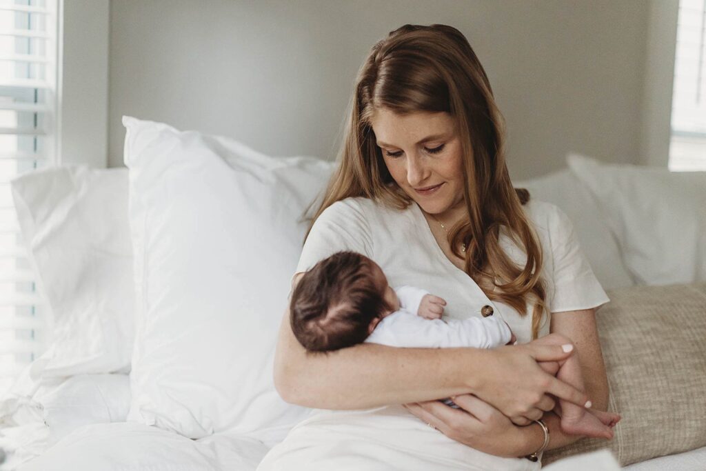 Mother holding her newborn baby wearing a white onesie at home in Atlanta.