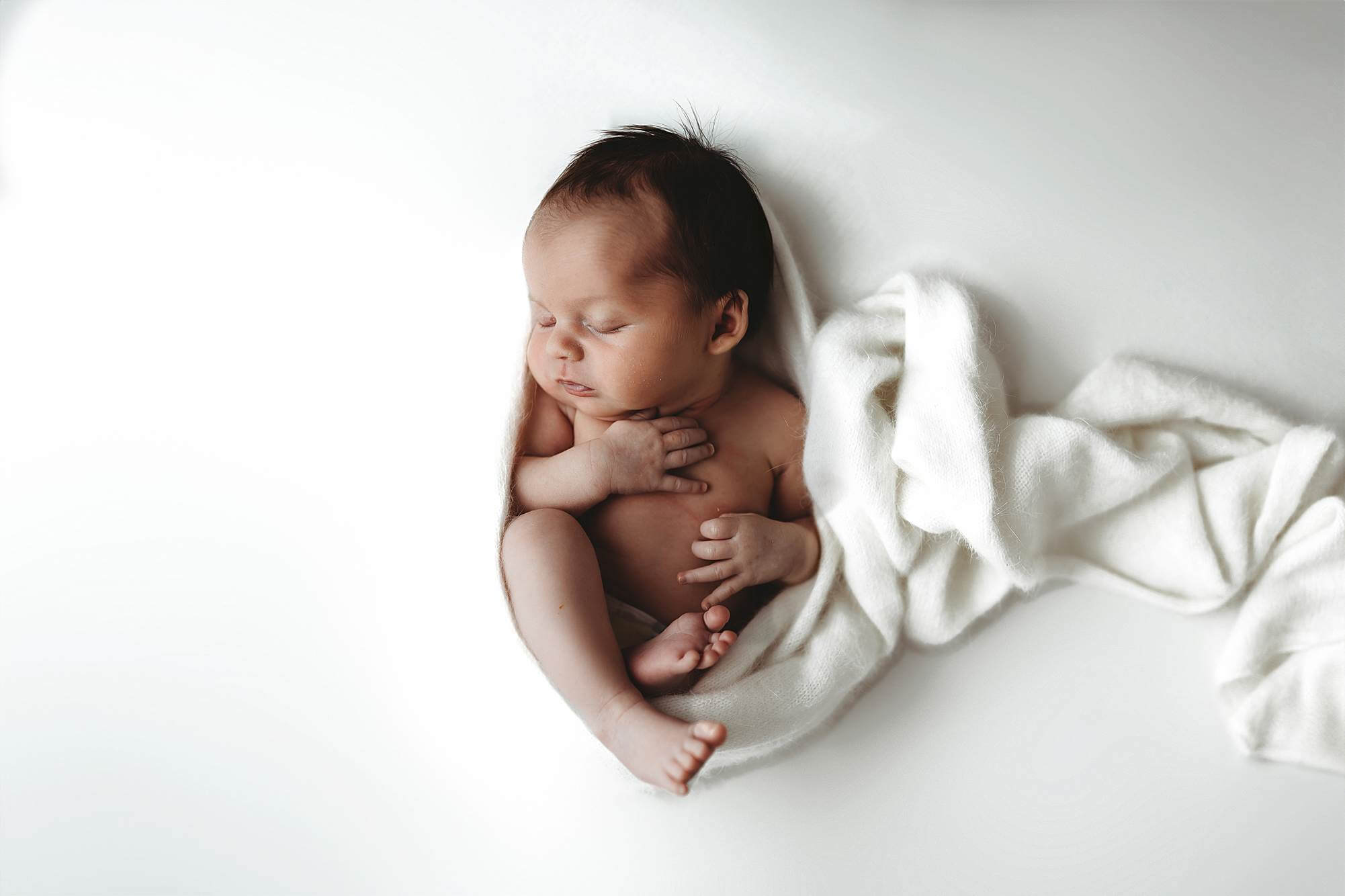 Newborn baby in a cozy womb-style pose wrapped in white fabric during an Atlanta posed newborn photography session.