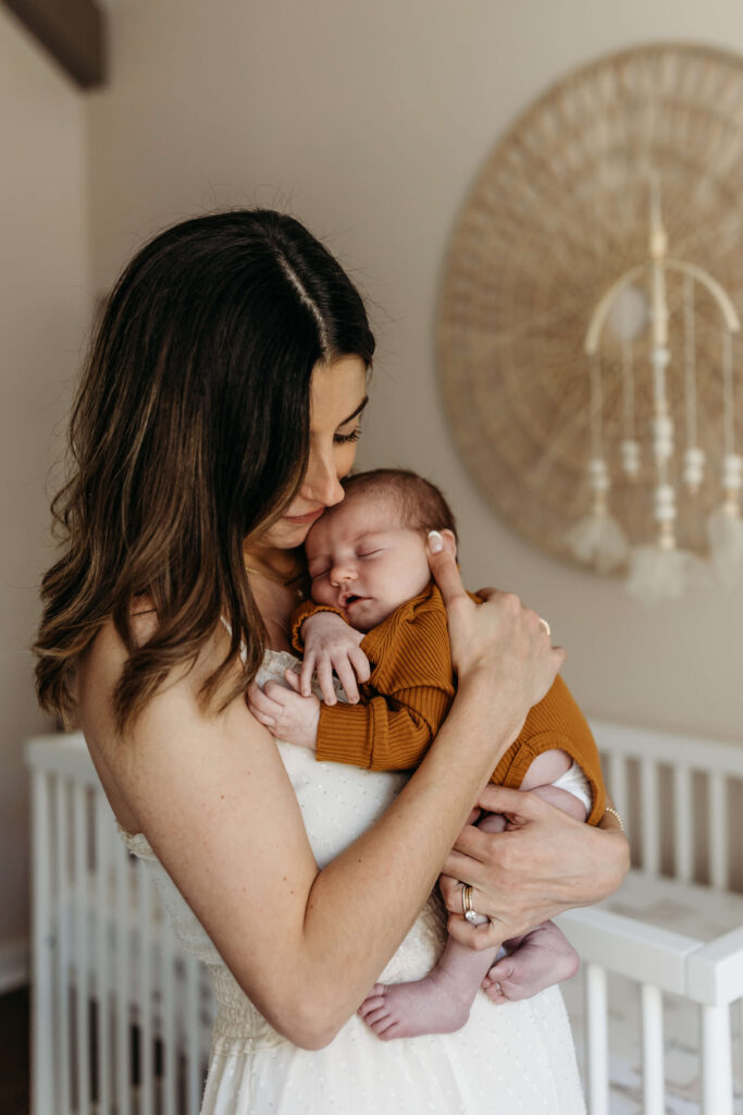 Mother snuggling her baby in a cozy boho-style nursery at home.