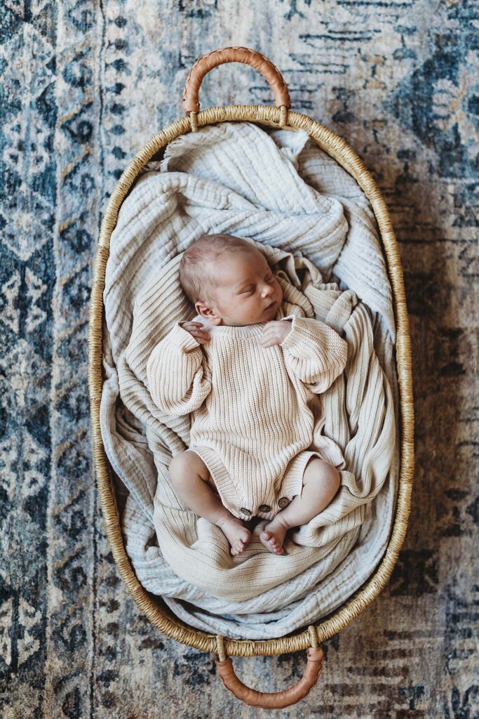 Newborn baby wearing a thick knit sweater resting in a Moses basket