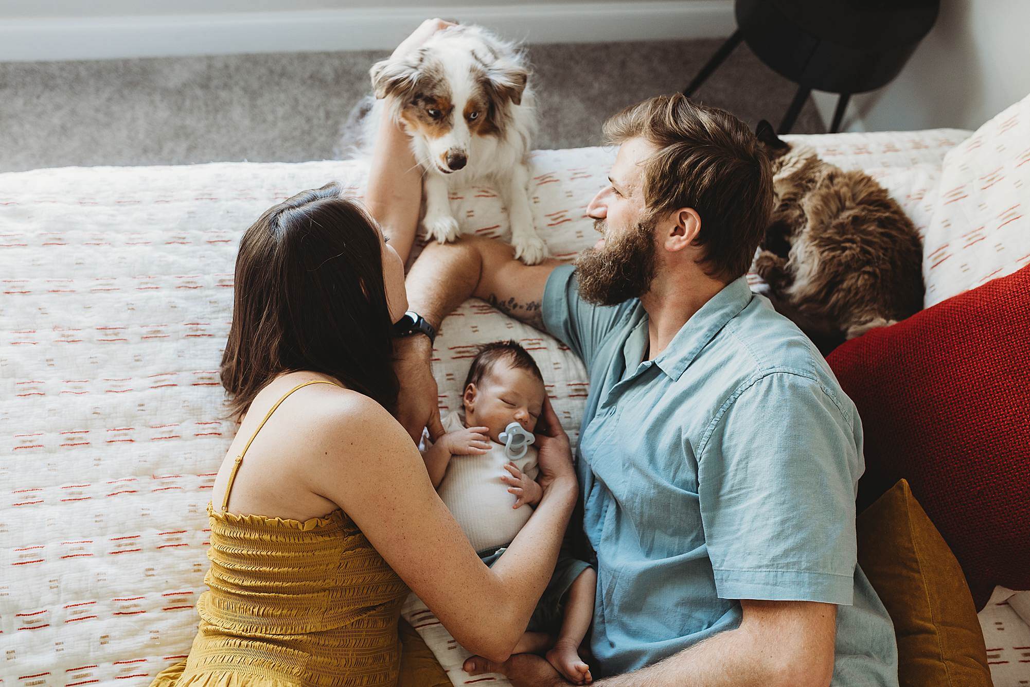 Parents lying on a bed with their newborn baby, cat, and dog during an in-home newborn photography session in Atlanta.